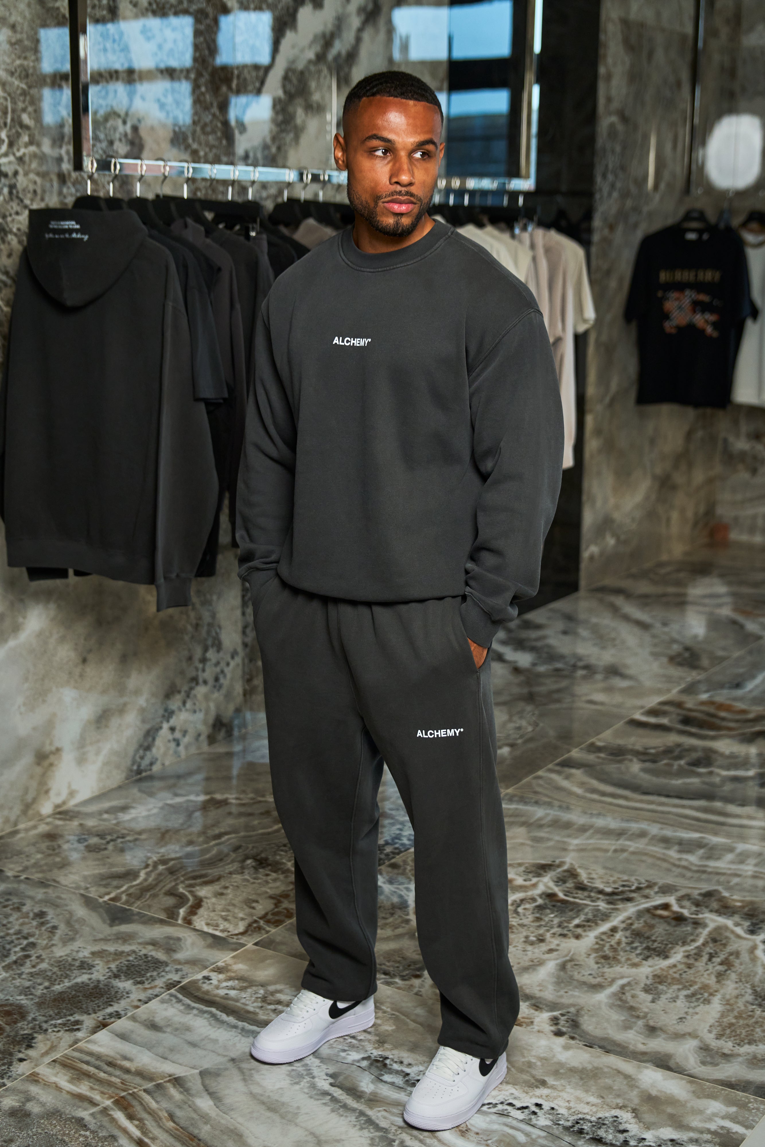 Man wearing a black tracksuit with ALCHEMY branding in a clothing store.