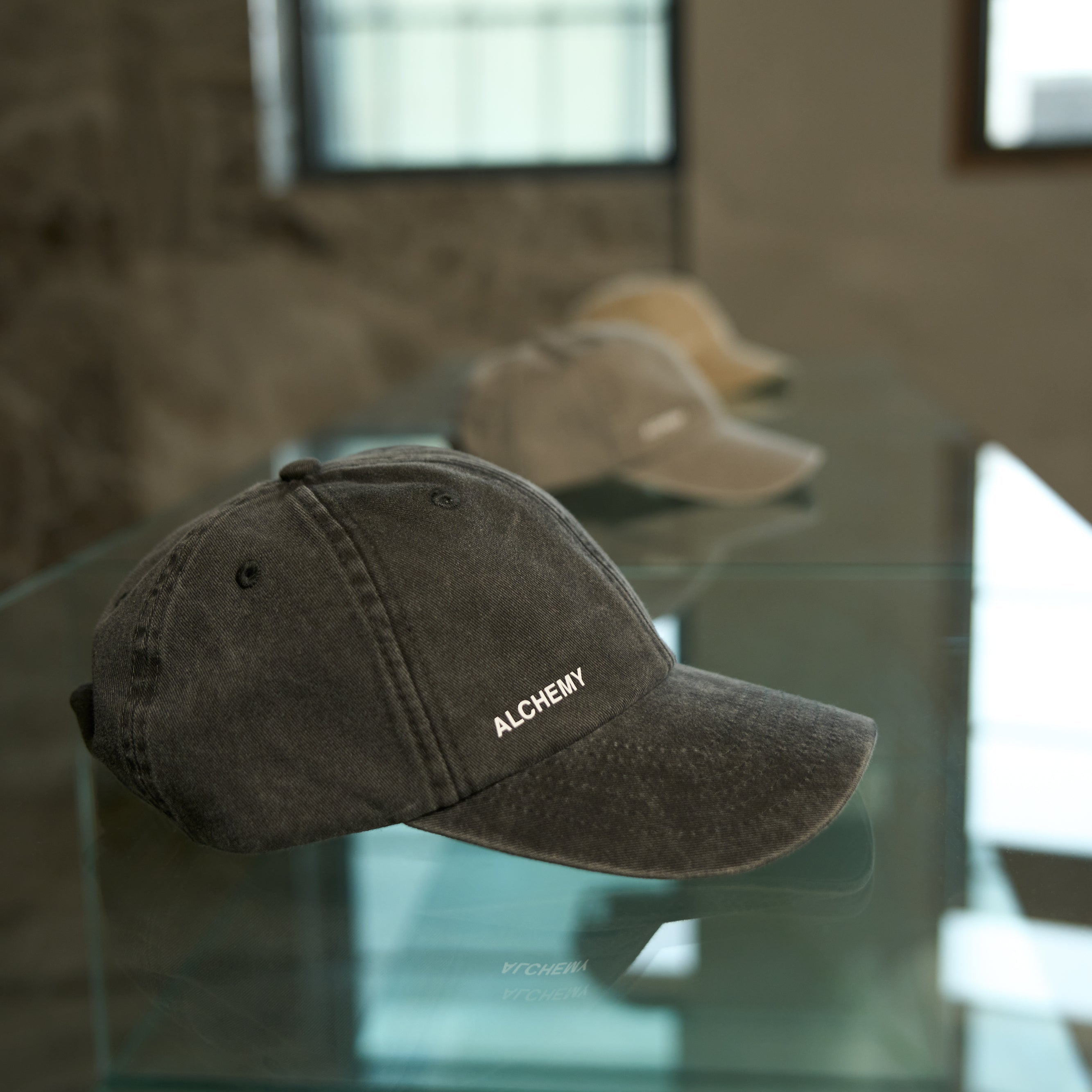 Gray cap with 'ALCHEMY' branding on a glass table