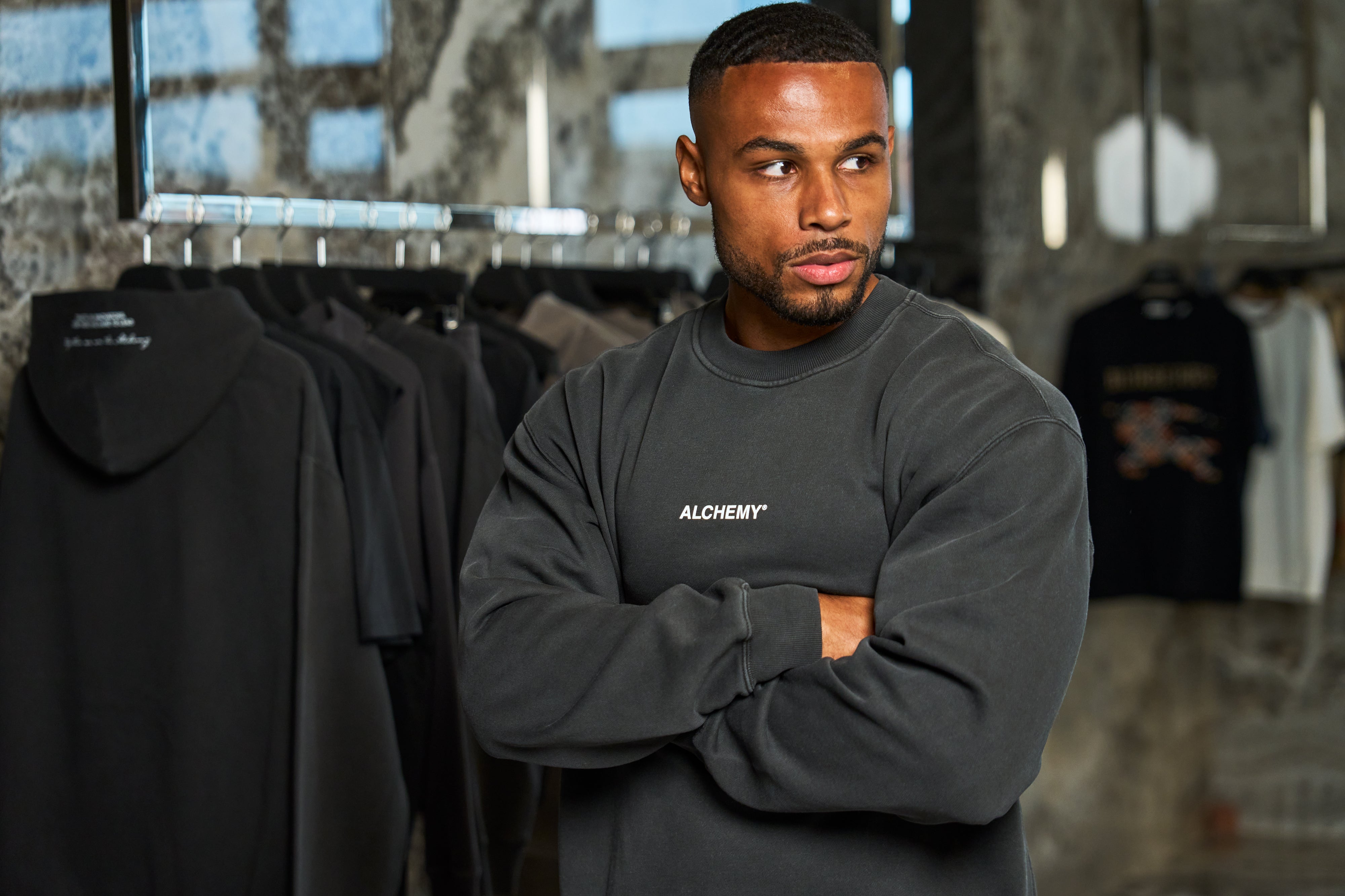 Man wearing a black sweatshirt with 'Alchemy' logo in a clothing store.